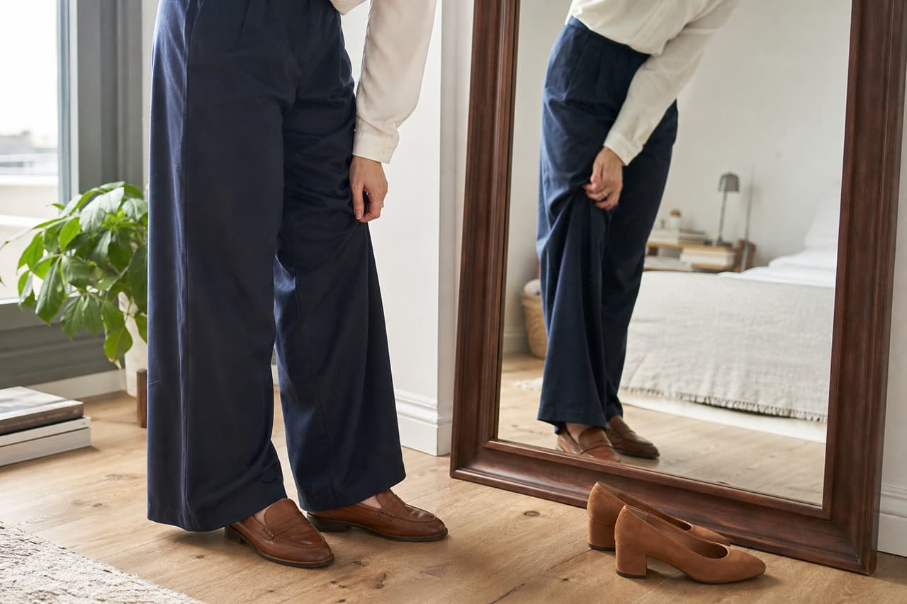 Mujer comparando el bajo de un pantalón azul marino con mocasines y zapatos de tacón bajo.