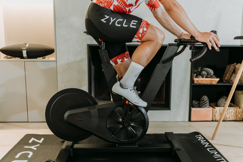 Detalle de una persona pedaleando en una bicicleta indoor conectada con ropa de ciclismo.
